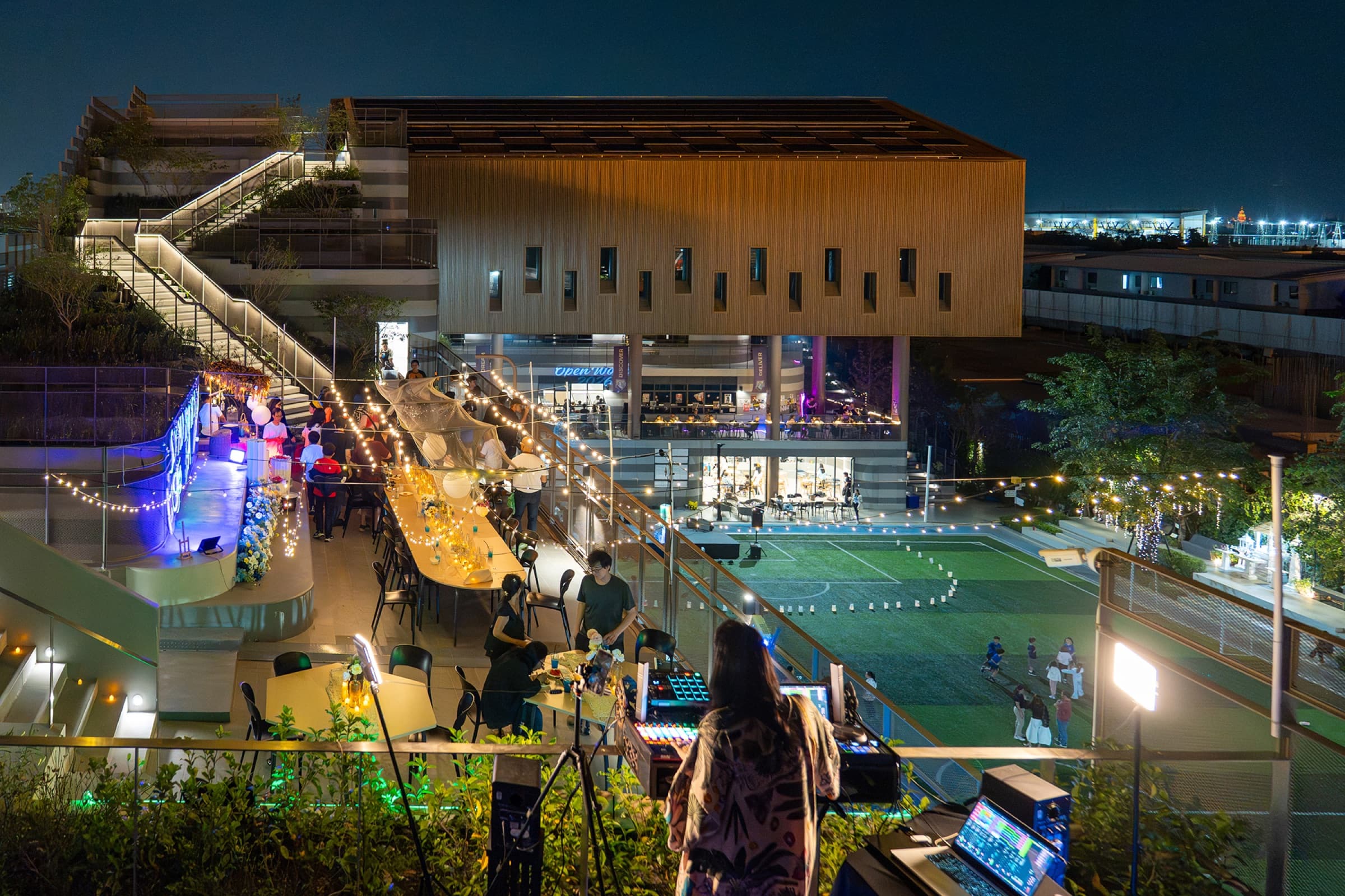 Open World 2026 at night on the school rooftop, string lights over long tables and a DJ booth