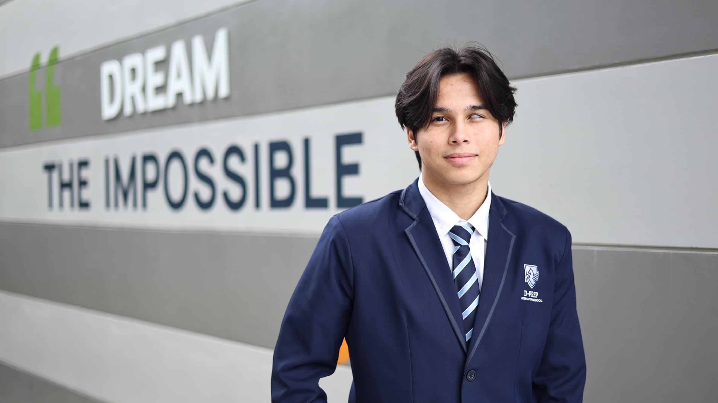 Victor in D-PREP school uniform in front of a Dream the Impossible wall